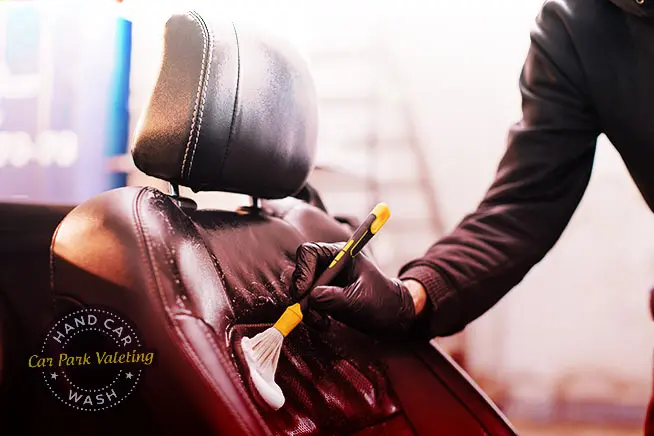 close up image of car wash attendant cleaning seats with brush on how to get paint out of car seat blog